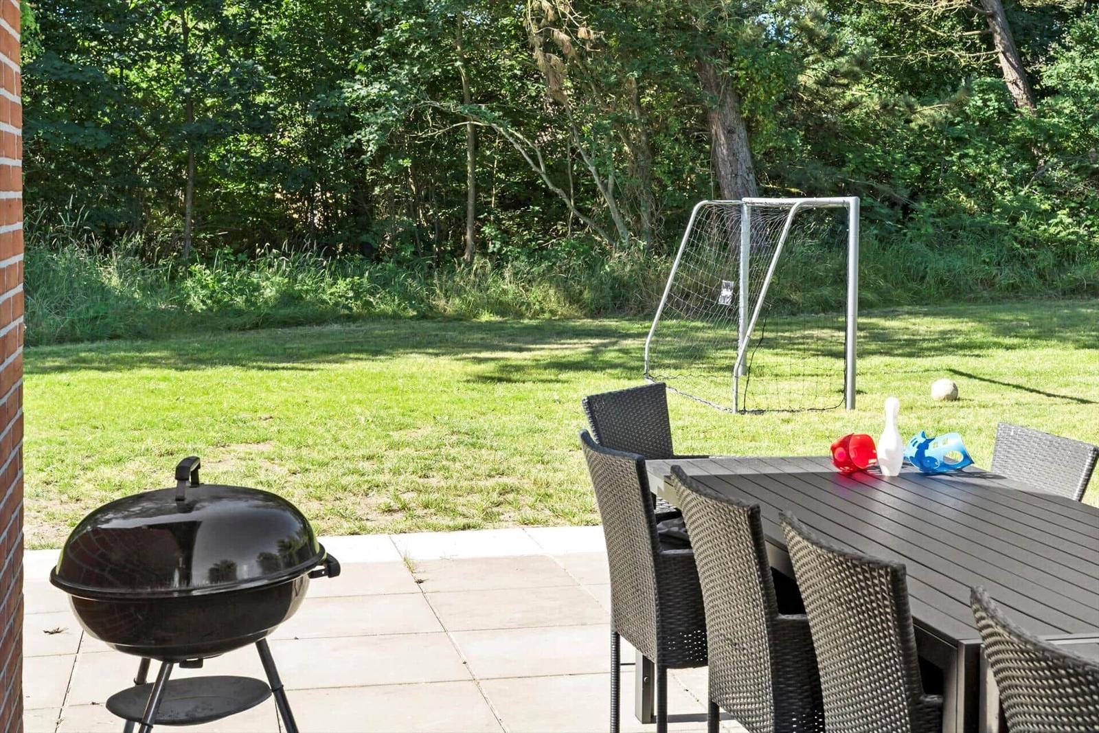 Terrasse mit Grill, Tisch und Stühlen. Im Hintergrund Fußballtor und Grasfläche.