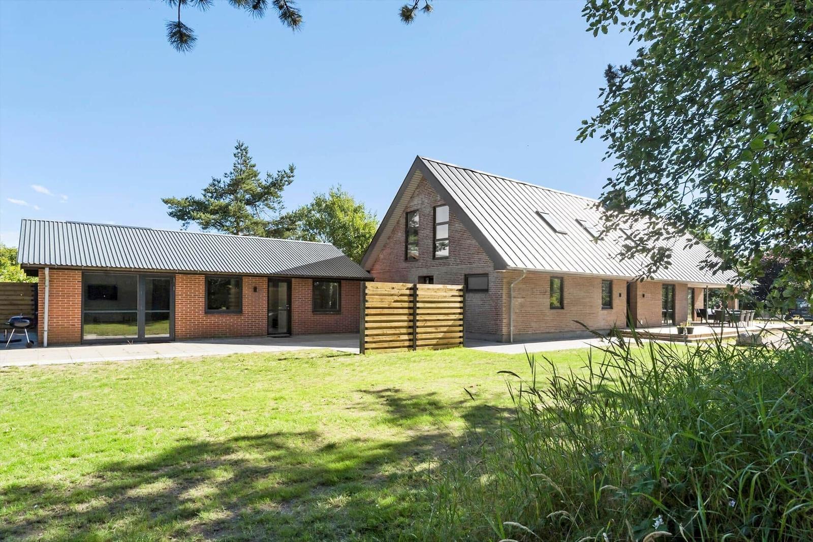 Moderne Villa mit Holz- und Ziegelbauweise, großem Garten und Terrasse unter blauem Himmel.