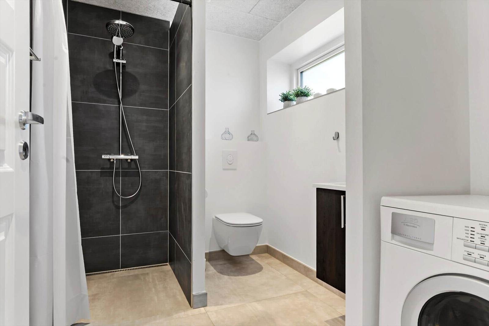 Dusche mit Duschbrause, WC und Waschmaschine im Bad.