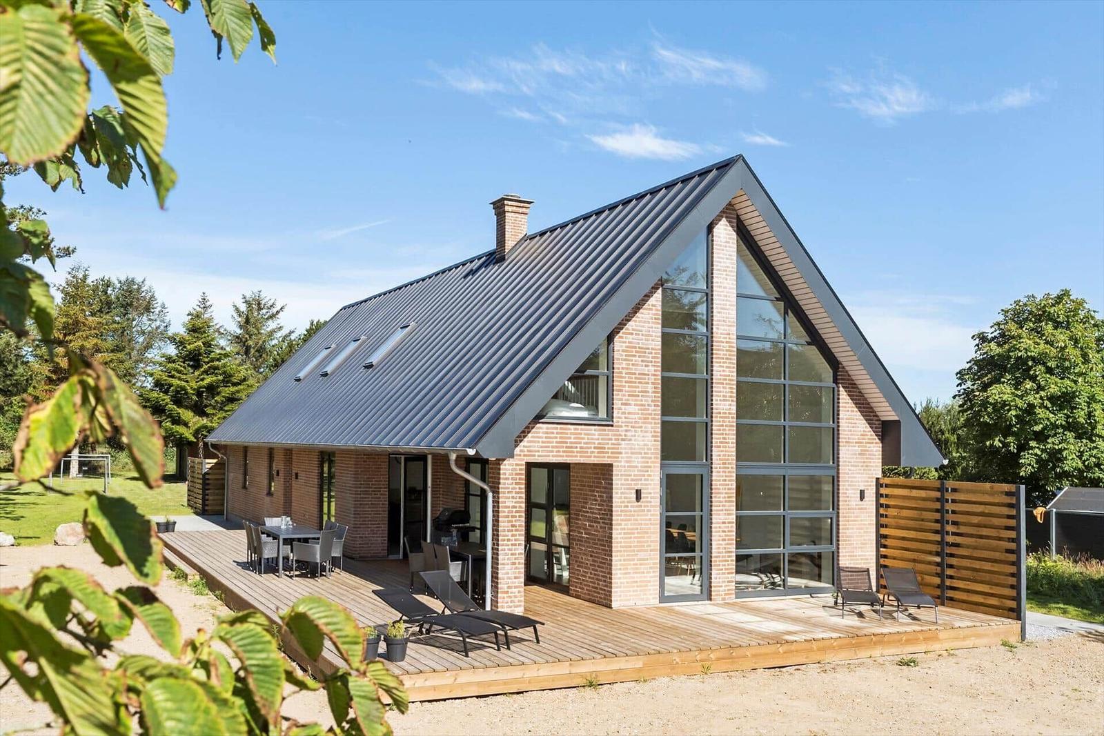 Moderne Villa mit Holzterrasse, Grill und großem Fensterbereich.