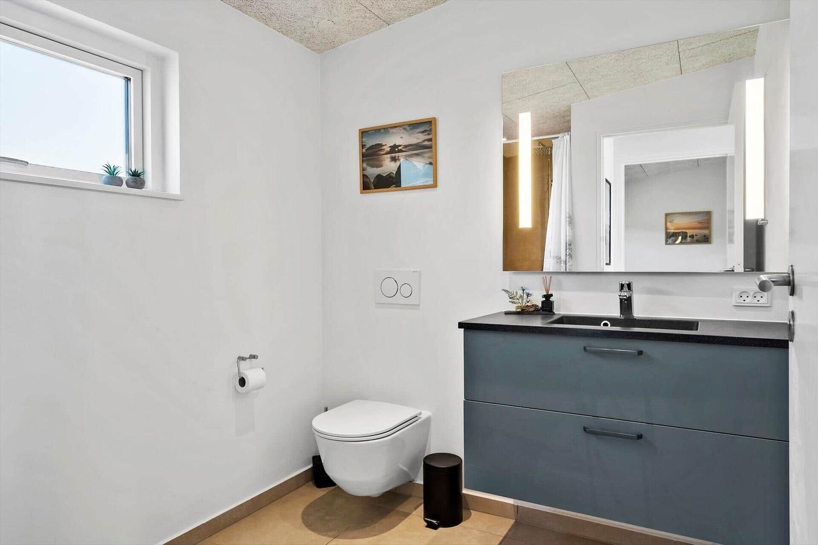 Badezimmer mit Toilette, Waschbecken und Spiegel. Fenster mit Pflanzen.