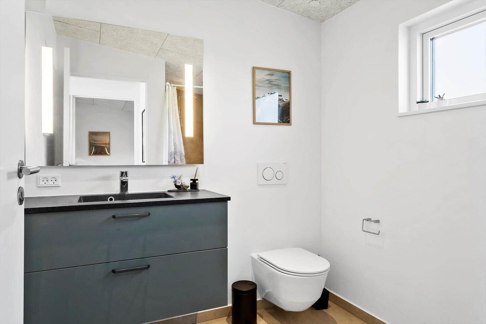 Badezimmer mit Waschbecken, Spiegel und Toilette. Fenster mit Pflanze.