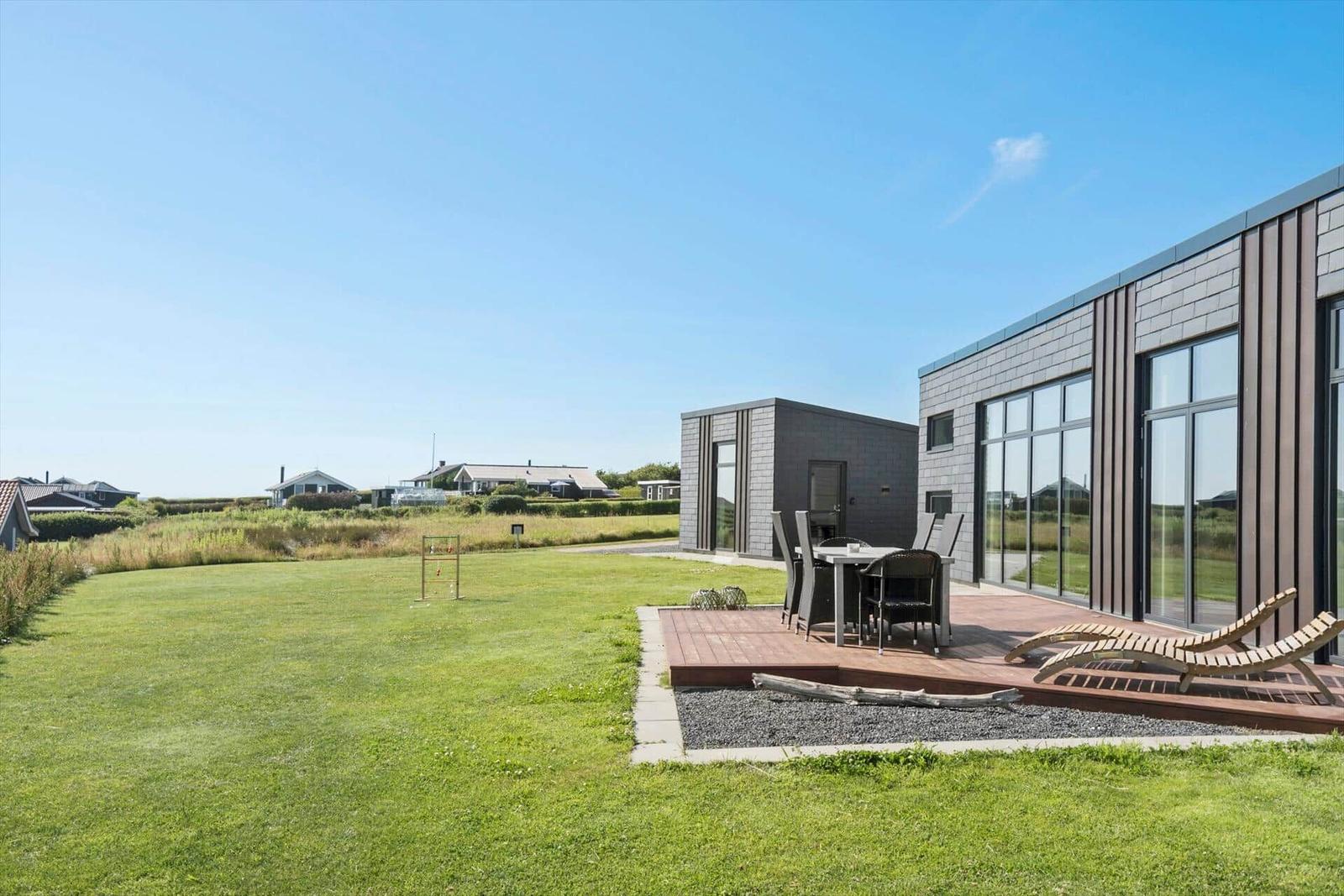 Moderne Villa mit Terrasse, Garten und Lounge-Bereich unter blauem Himmel.