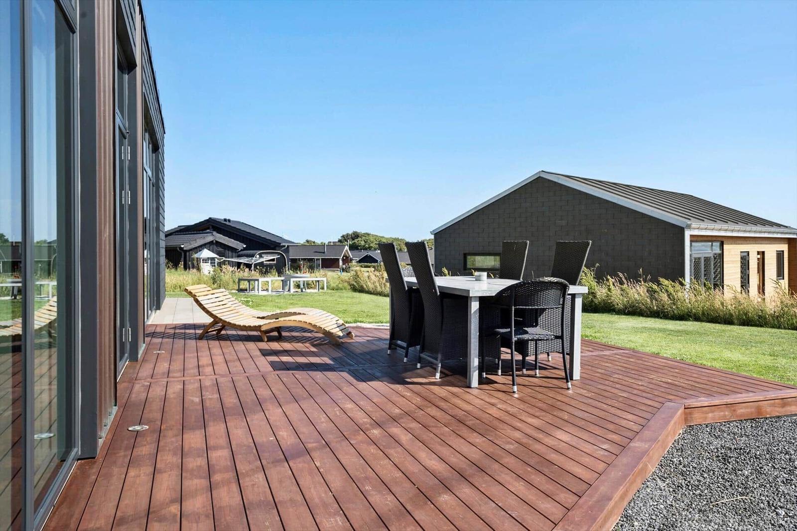 Terrasse mit Tisch, Stühlen und Liegestuhl. Blick auf Grünfläche und Nachbarhäuser.