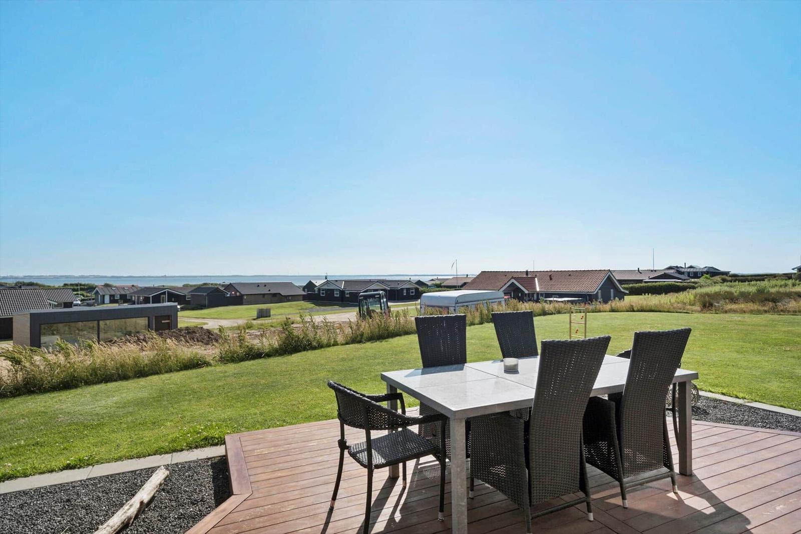 Terrasse mit Tisch und Stühlen, Blick auf Grasfläche und Ferienhäuser.