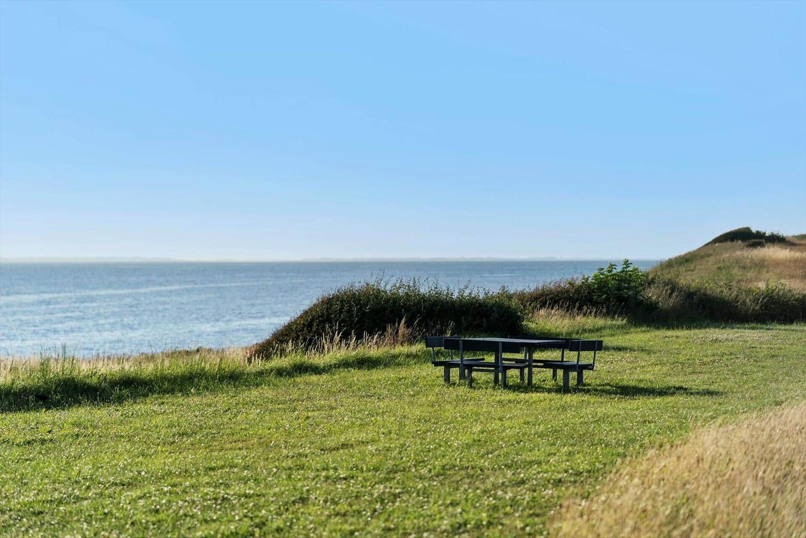 Ein schwarzer Tisch mit Bänken auf einer grünen Wiese mit Blick auf das Meer.