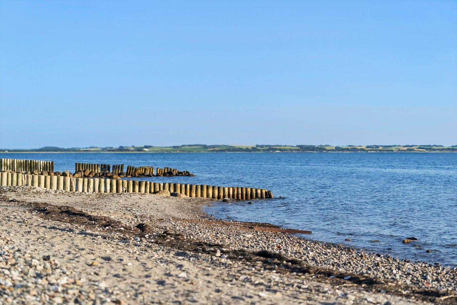 Steiniger Strand mit Holzpfählen am Wasser, Blick auf die gegenüberliegende Küstenlinie.
