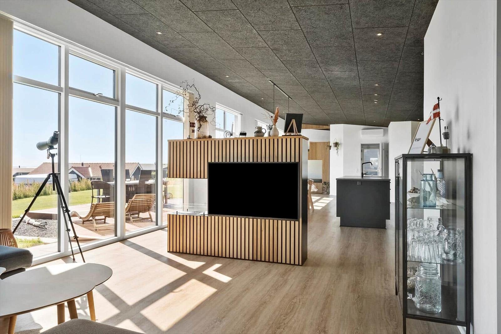 Großes Wohnzimmer mit Fernseher, Glasfront und Küchenbereich.