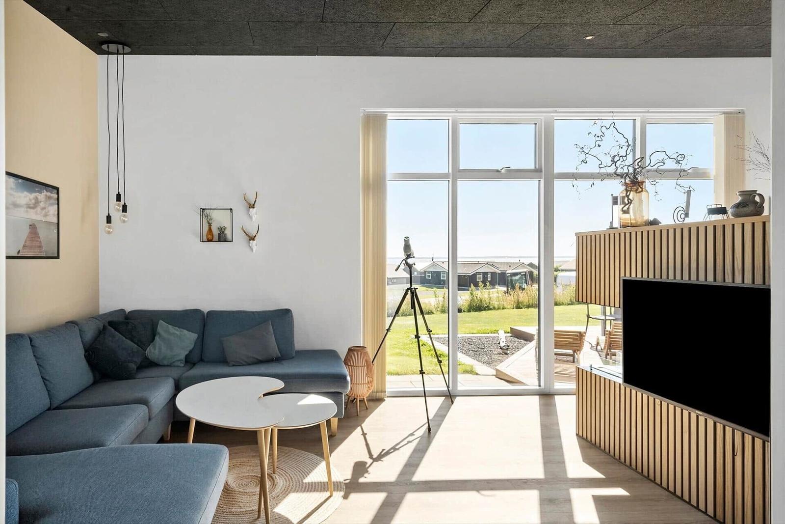 Wohnzimmer mit Sofa, Couchtisch und TV. Große Fenster bieten Blick auf Garten.