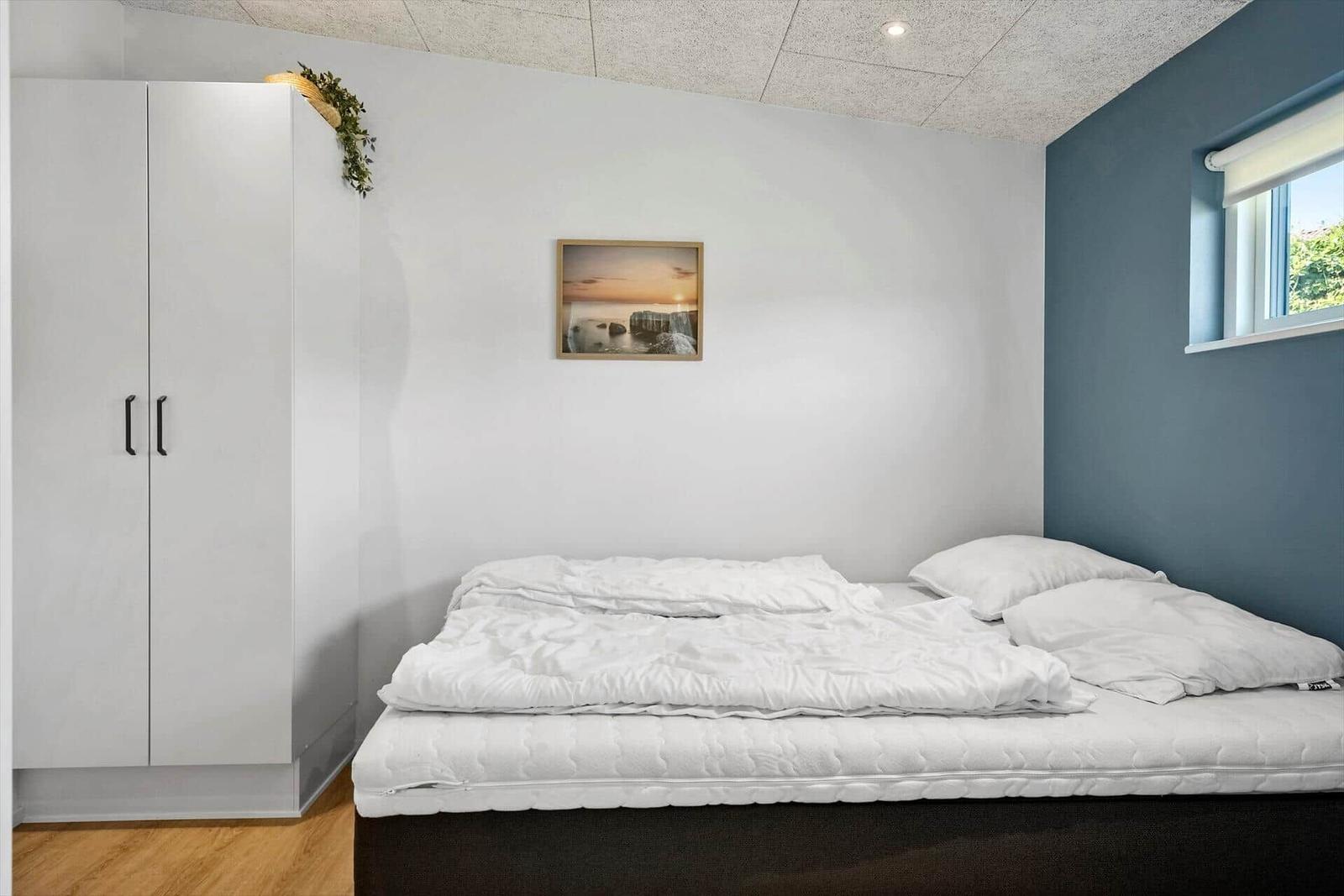 Schlafzimmer mit Bett, Kleiderschrank und Fenster.