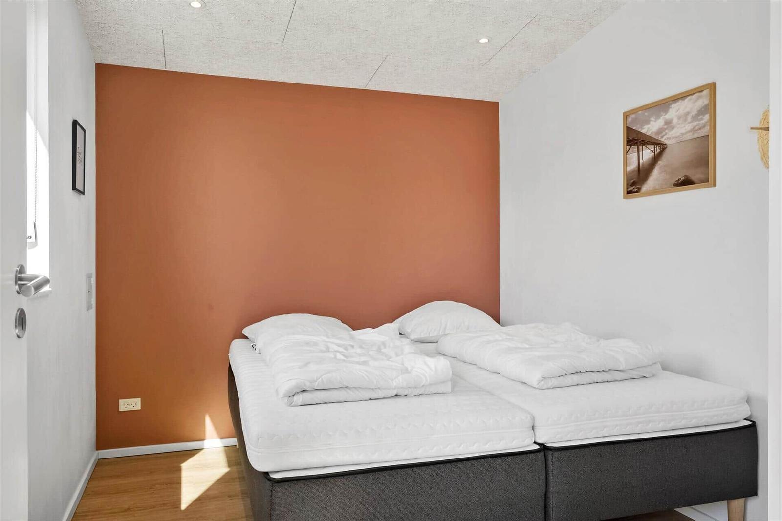 Zimmer mit zwei Matratzen, orange Wand, weißer Bettwäsche und Holzboden.