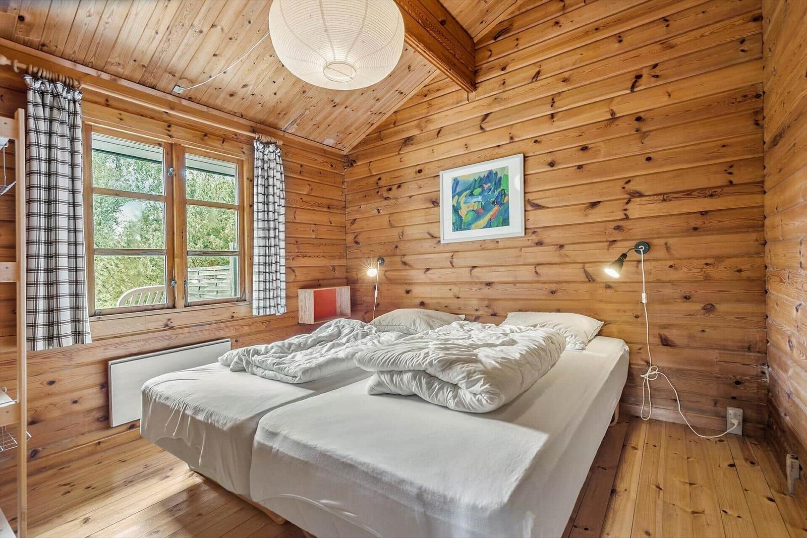 Bedroom with wooden walls, double bed, and window with view.