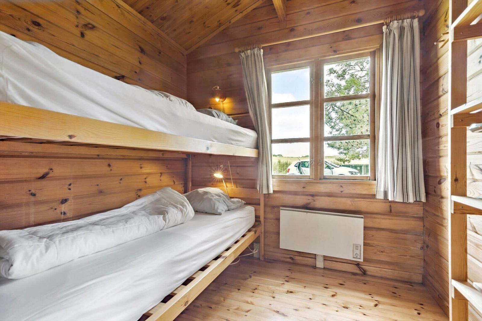 Room with bunk beds, wooden walls, and window with view outside.