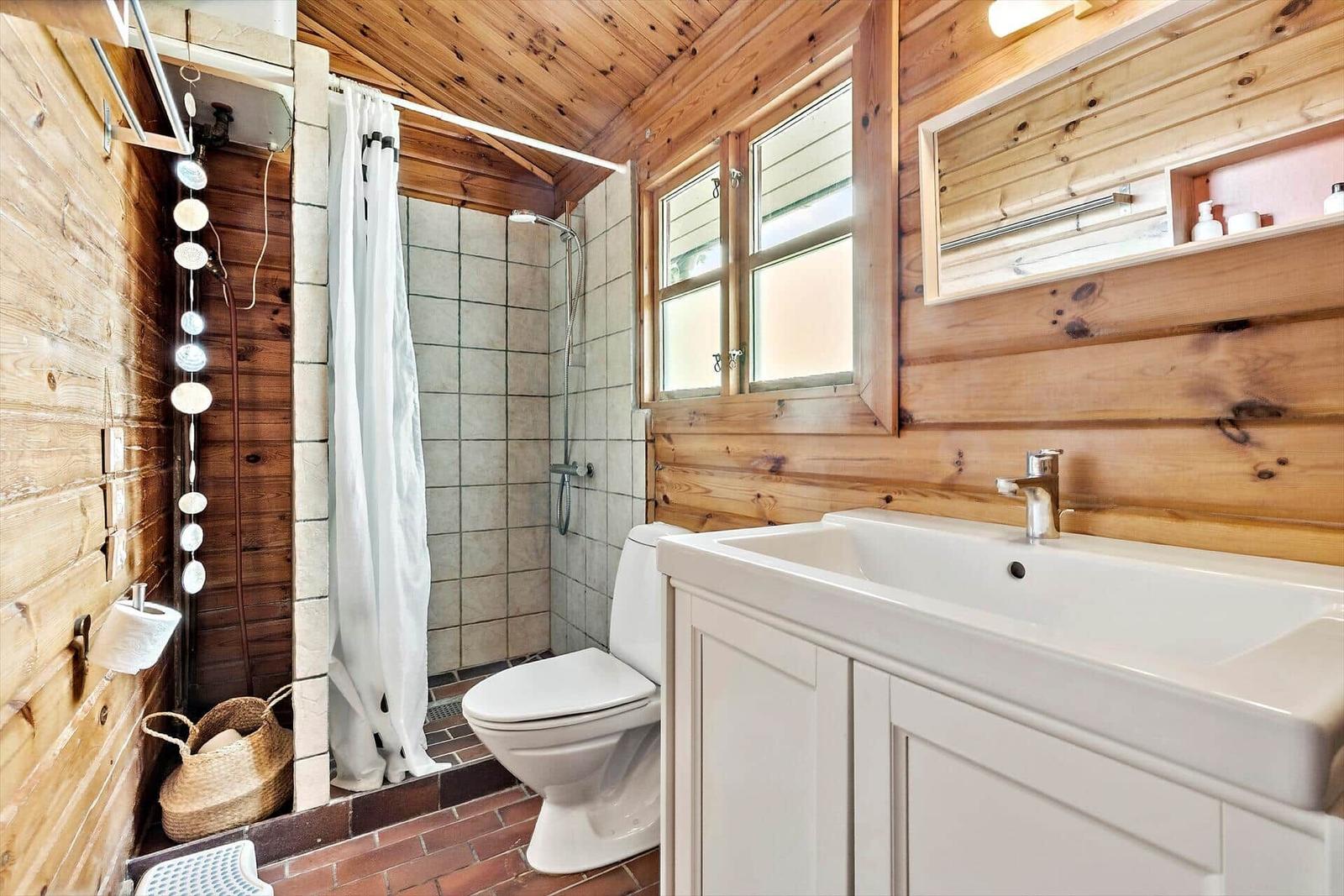 Bathroom with shower, toilet, and sink. Wooden walls and window.