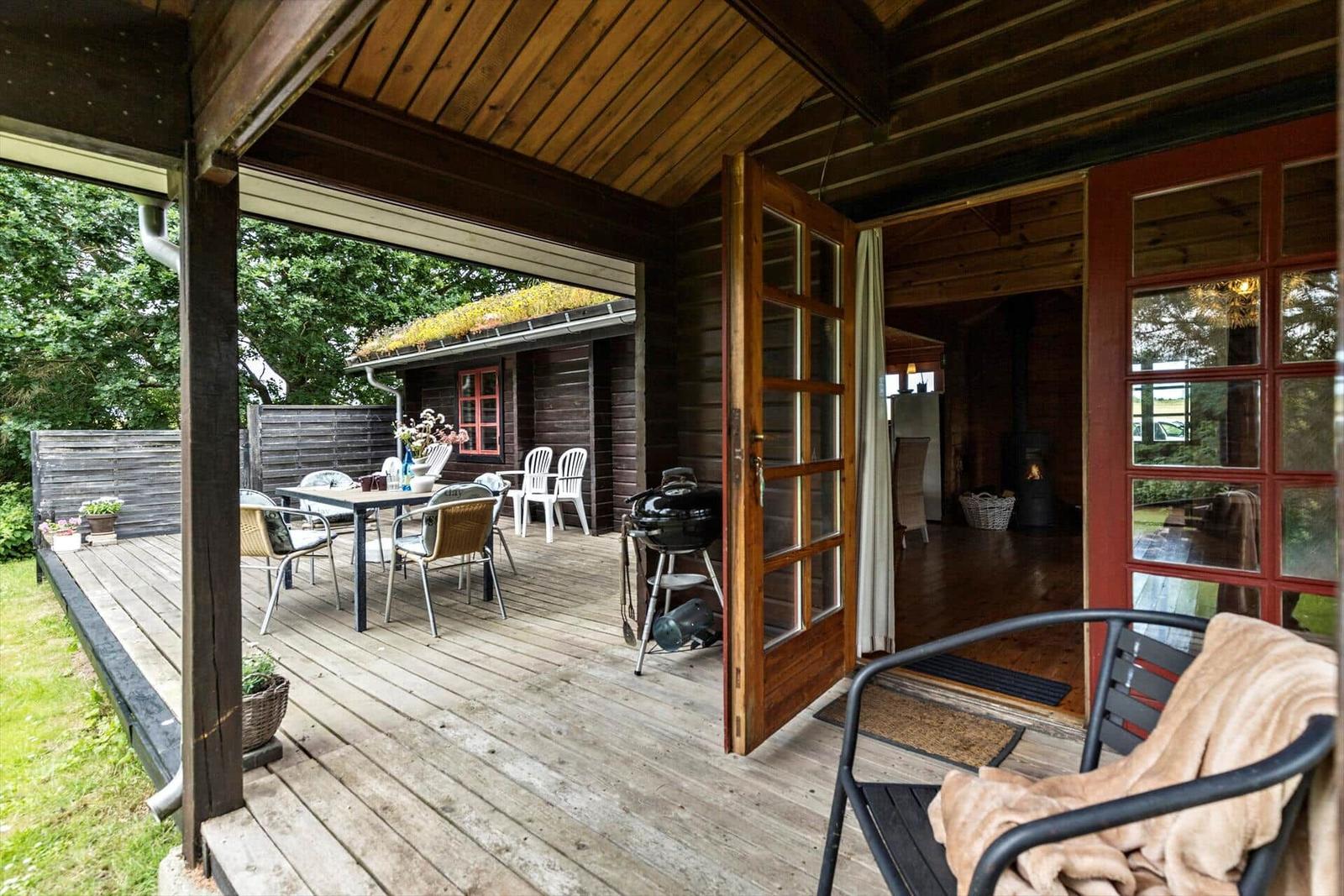 Deck with table, chairs, and grill. Wooden house with open entrance.