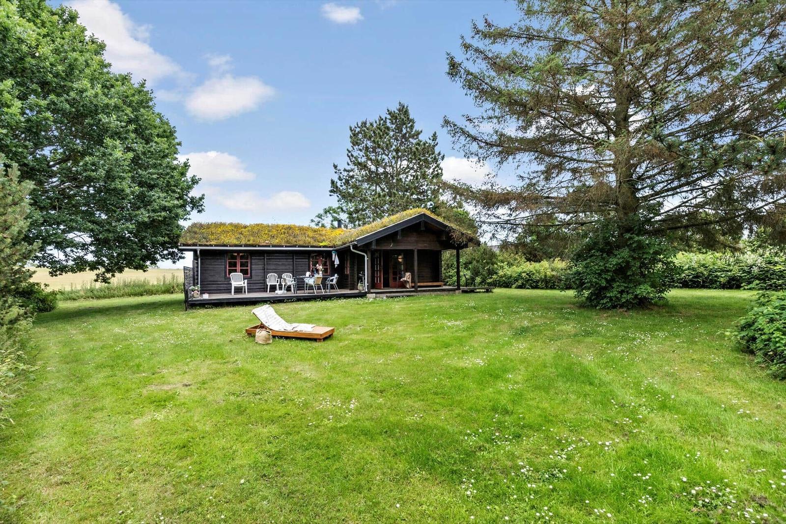 Wooden cabin with green roof, terrace and garden. Lounge chair on lawn.