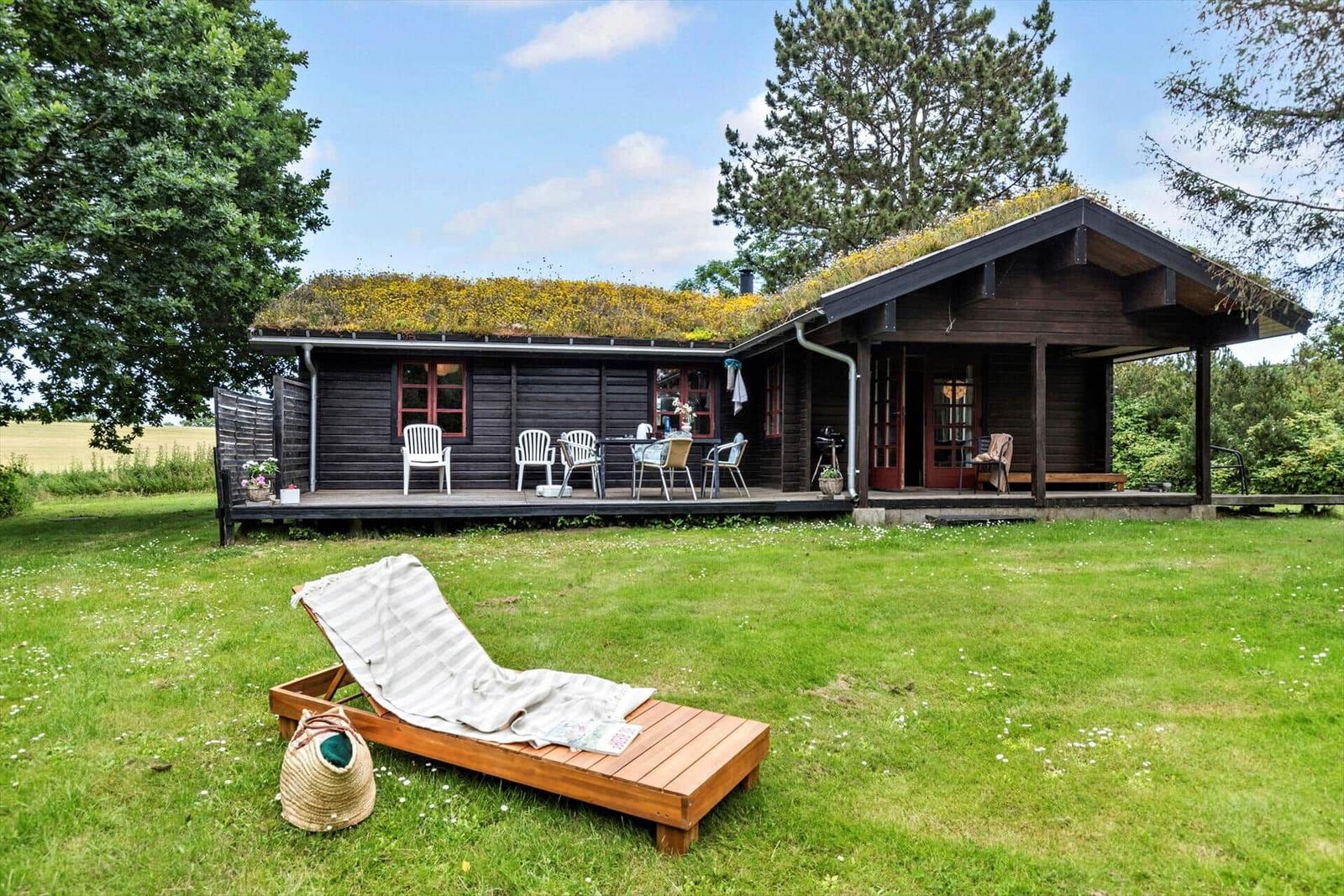 Wooden house with grass roof, terrace, and lounge chair in the garden.