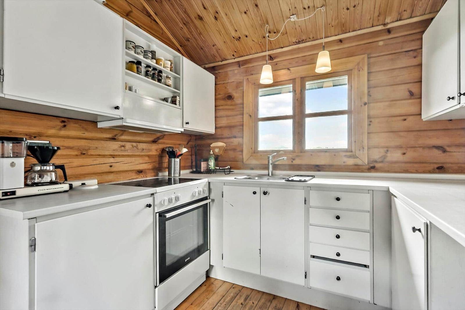 Kitchen with white cabinets, wooden walls, and window. Countertop, sink, and stove are present.