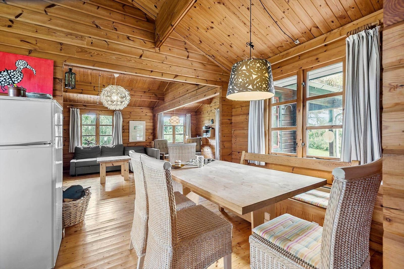 Dining area with wooden table and chairs, view into living room with sofa and windows.