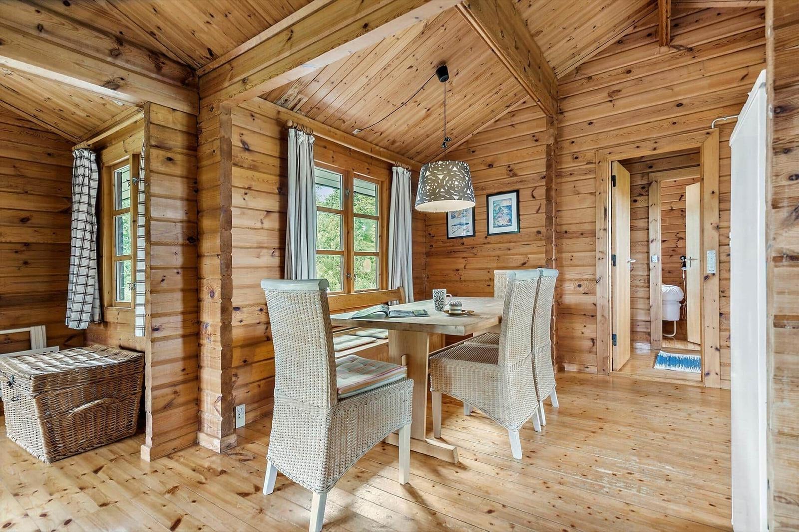 Dining room with wooden walls, table and chairs. View to bathroom and windows.