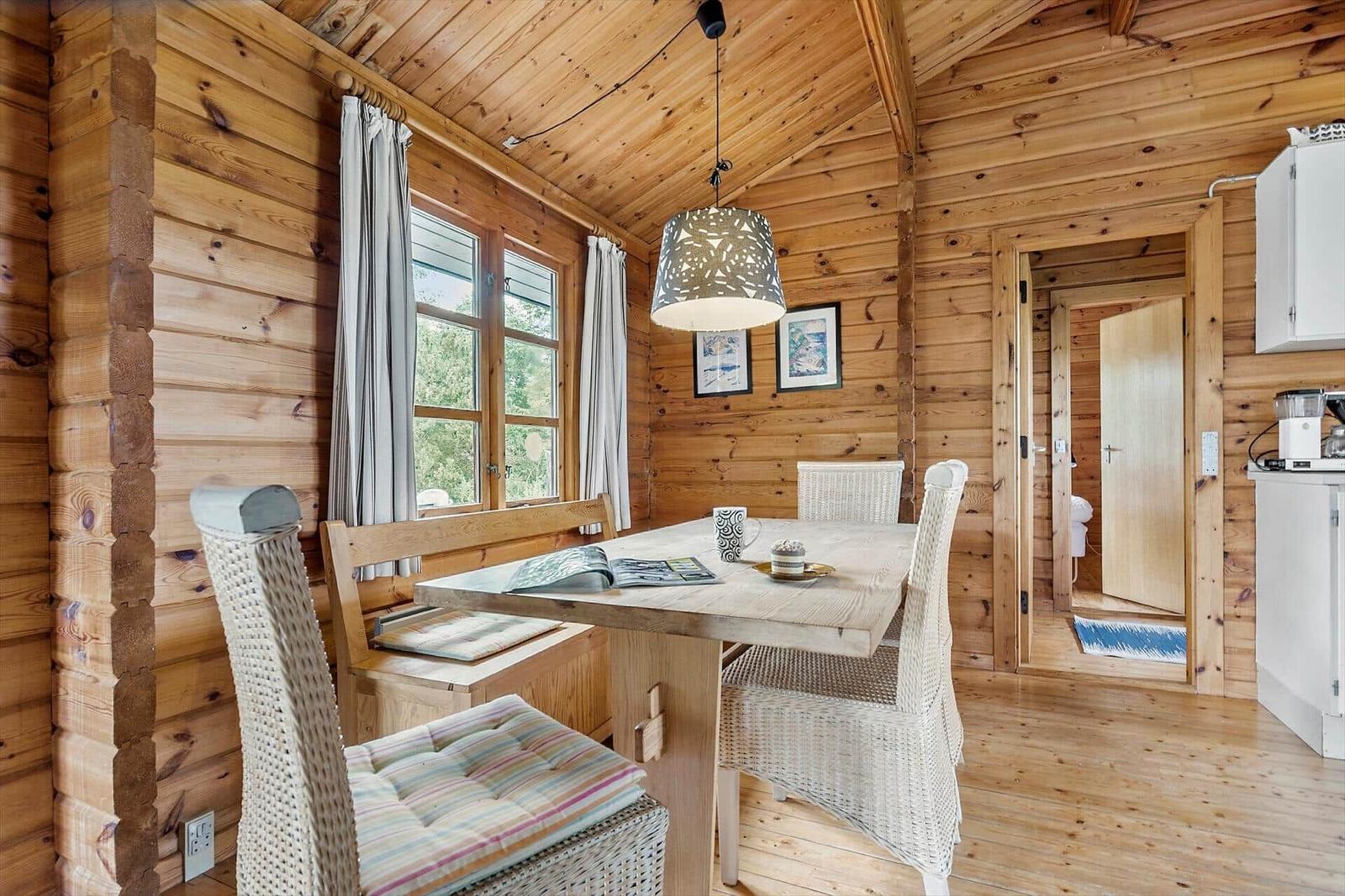 Dining area with wooden walls and table with chairs. Passage to toilet on the right.