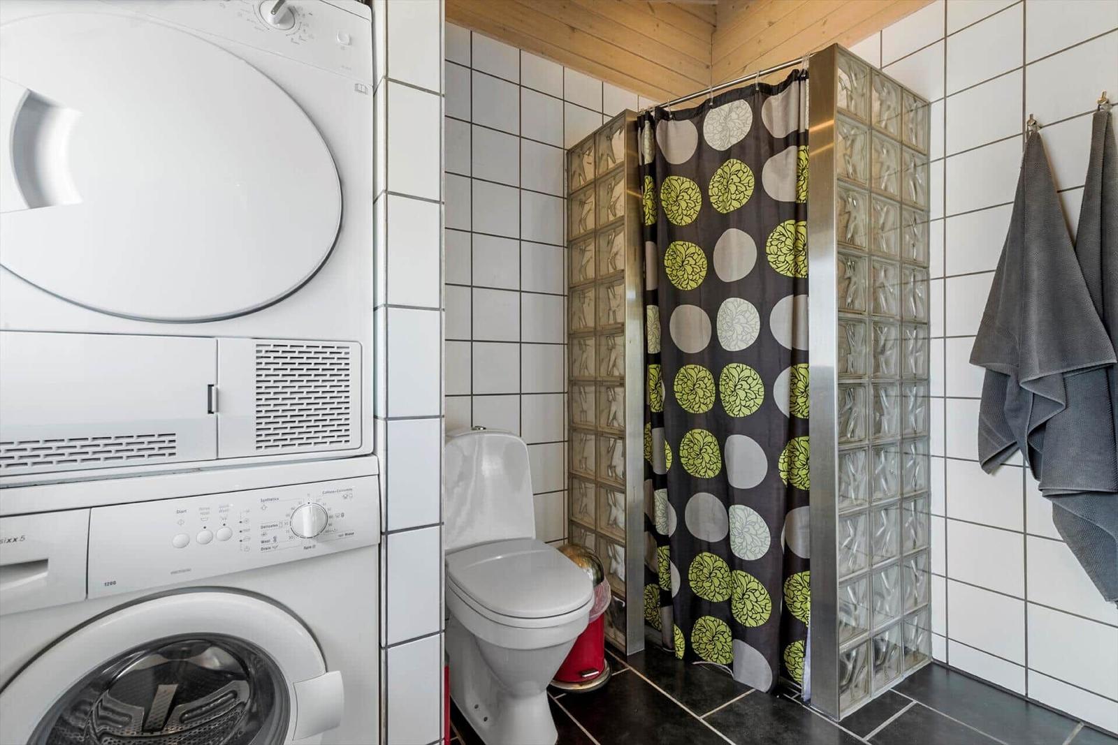 Badezimmer mit Waschmaschine, Toilette und Dusche mit Glasblockwand.