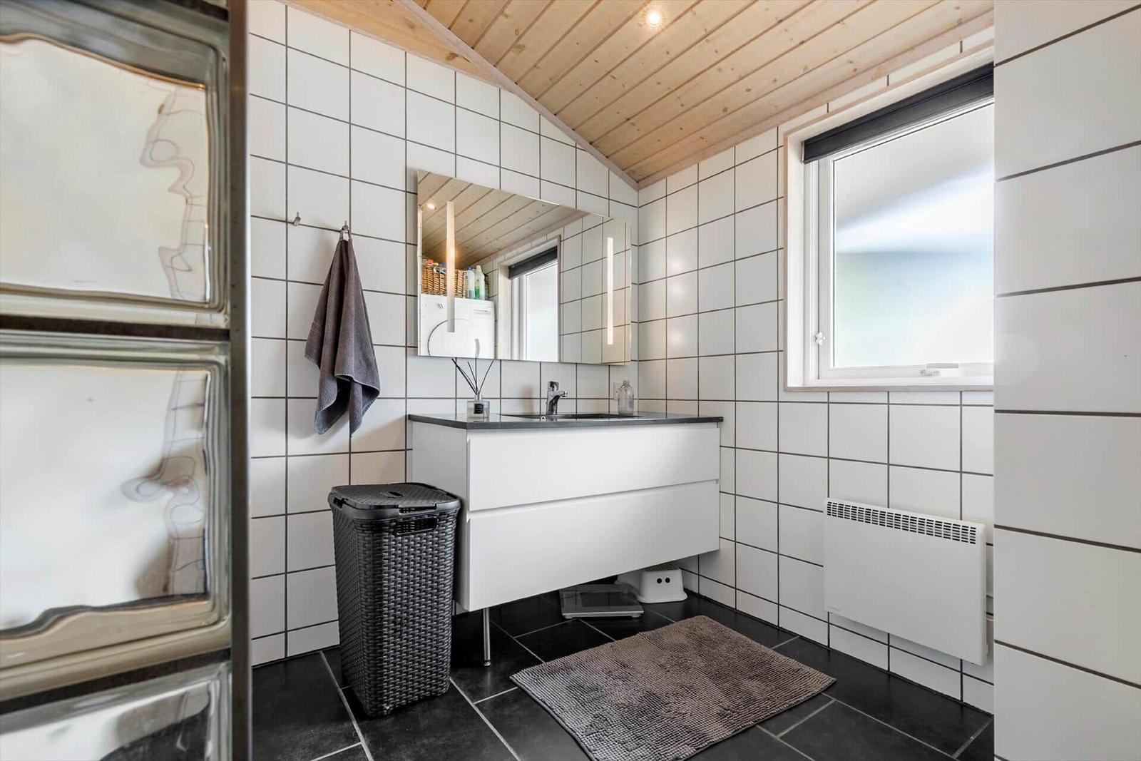 Badezimmer mit Waschbecken, Spiegel und Fenster. Fliesenwand und Holzdecke.
