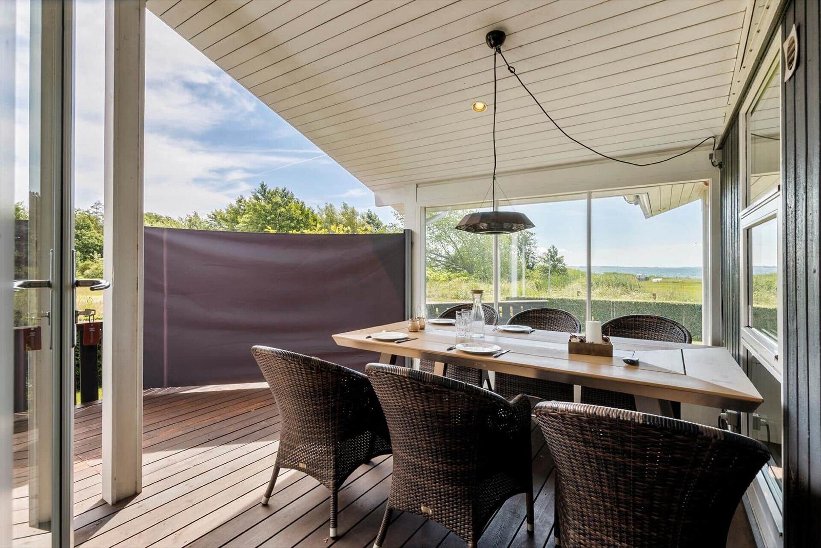 Terrasse mit Esstisch und Stühlen, Blick auf Grünflächen und Wasser.