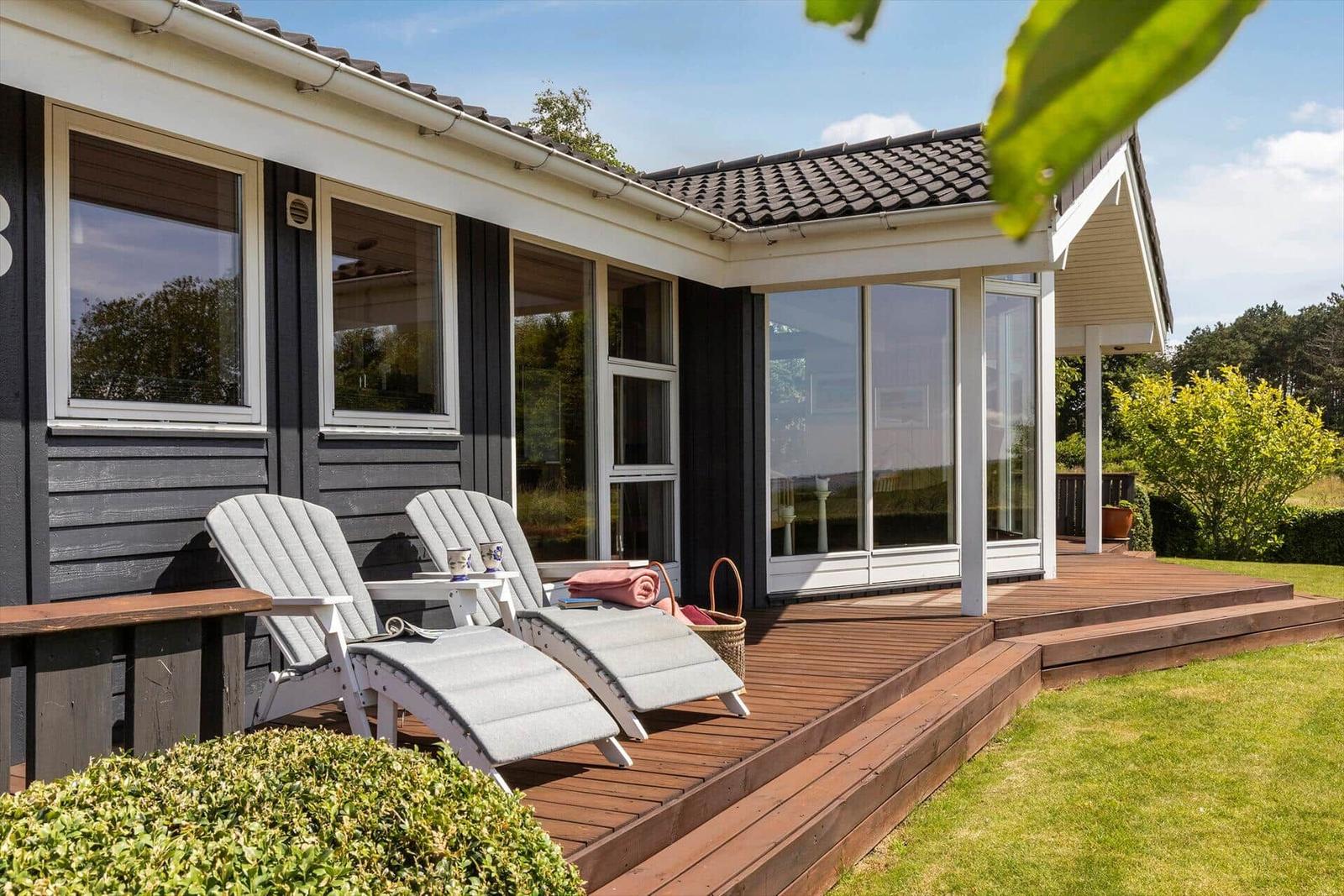 Terrasse mit Liegestühlen und Holzdecke vor einem Haus mit großen Fenstern.