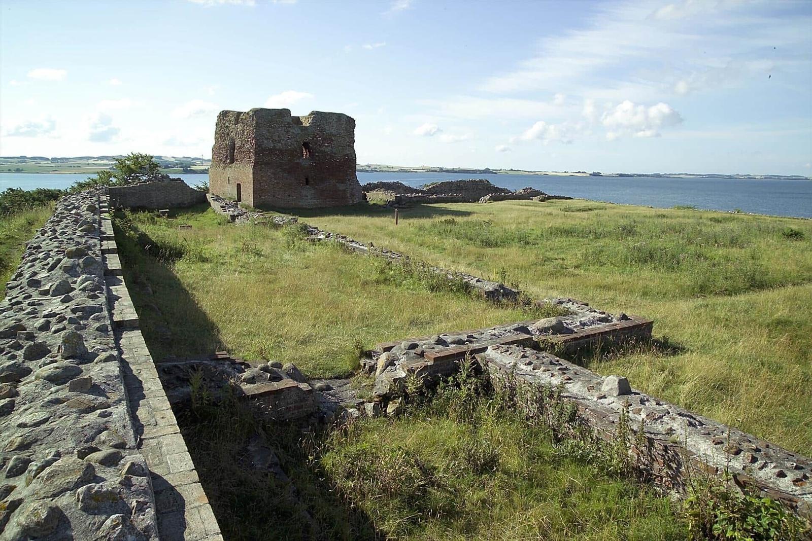 Ruinen einer alten Burg mit Blick aufs Meer und grüne Wiesen.