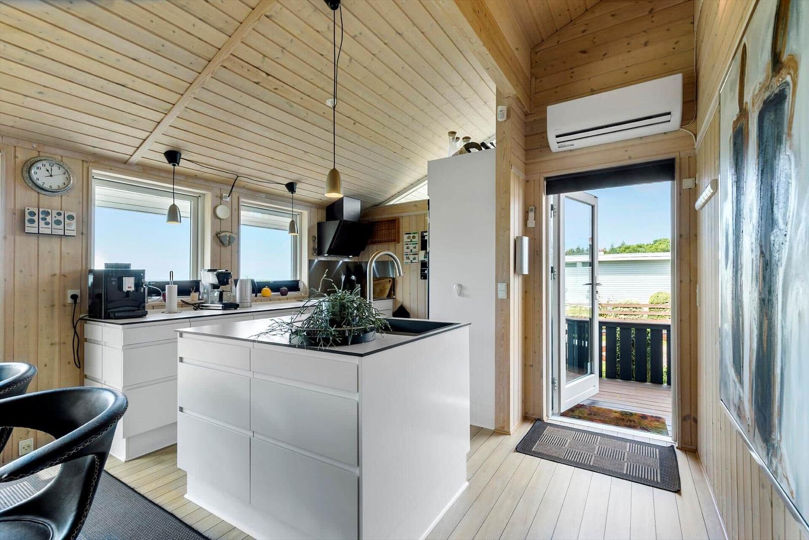 Küche mit weißem Küchenblock und Holzdecke. Tür führt auf Balkon.