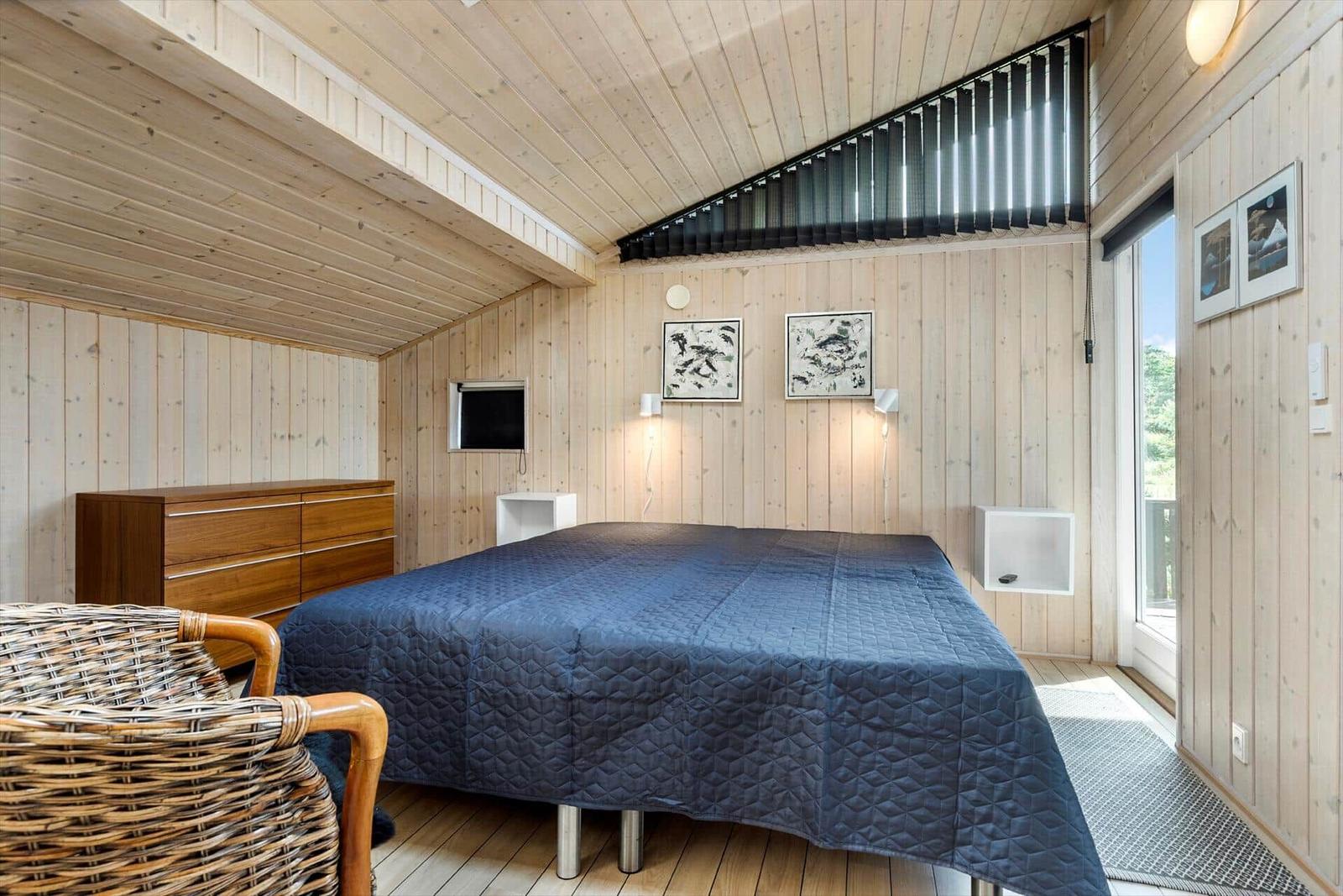 Schlafzimmer mit Holzwand, Bett, Schrank und Sicht auf Balkon.