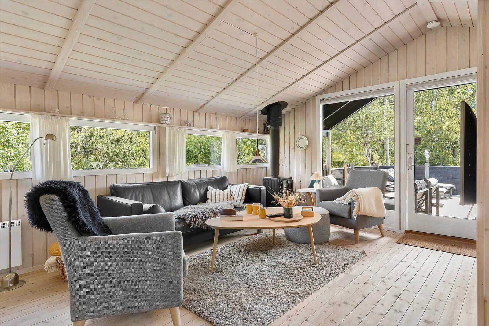Wohnzimmer mit Sofa, Sesseln und Holzboden. Durchgang zur Terrasse mit Gartenblick.