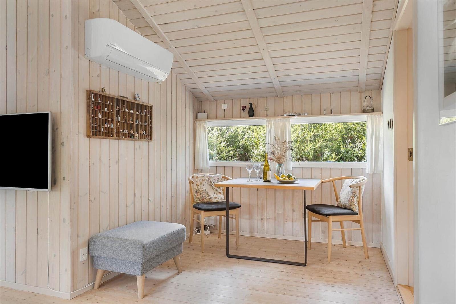 Essbereich mit Tisch, zwei Stühlen und Fenster. Wand mit Fernseher und Klimaanlage.