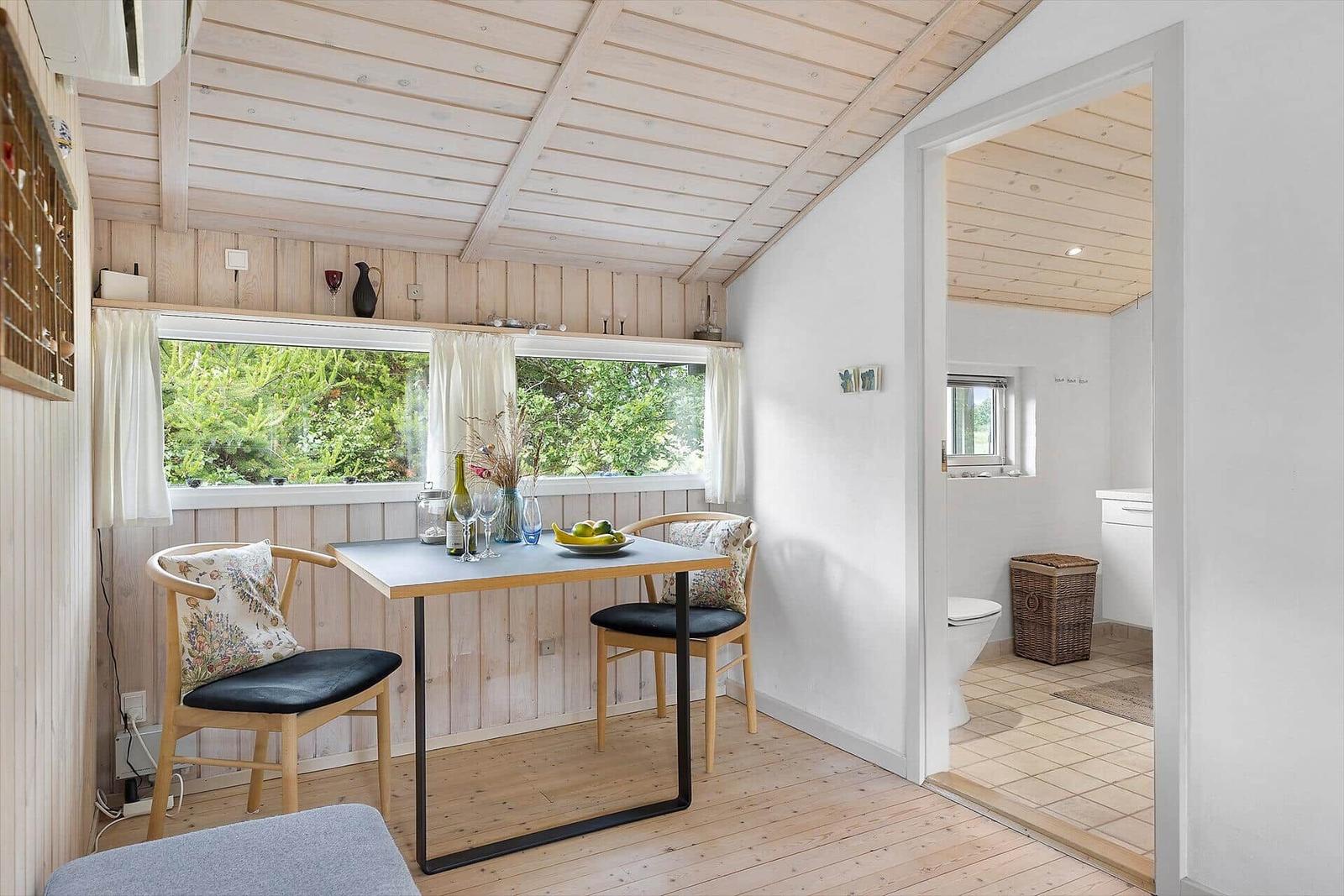 Essbereich mit Tisch, zwei Stühlen und Blick auf Grün. Durchgang in die Toilette.