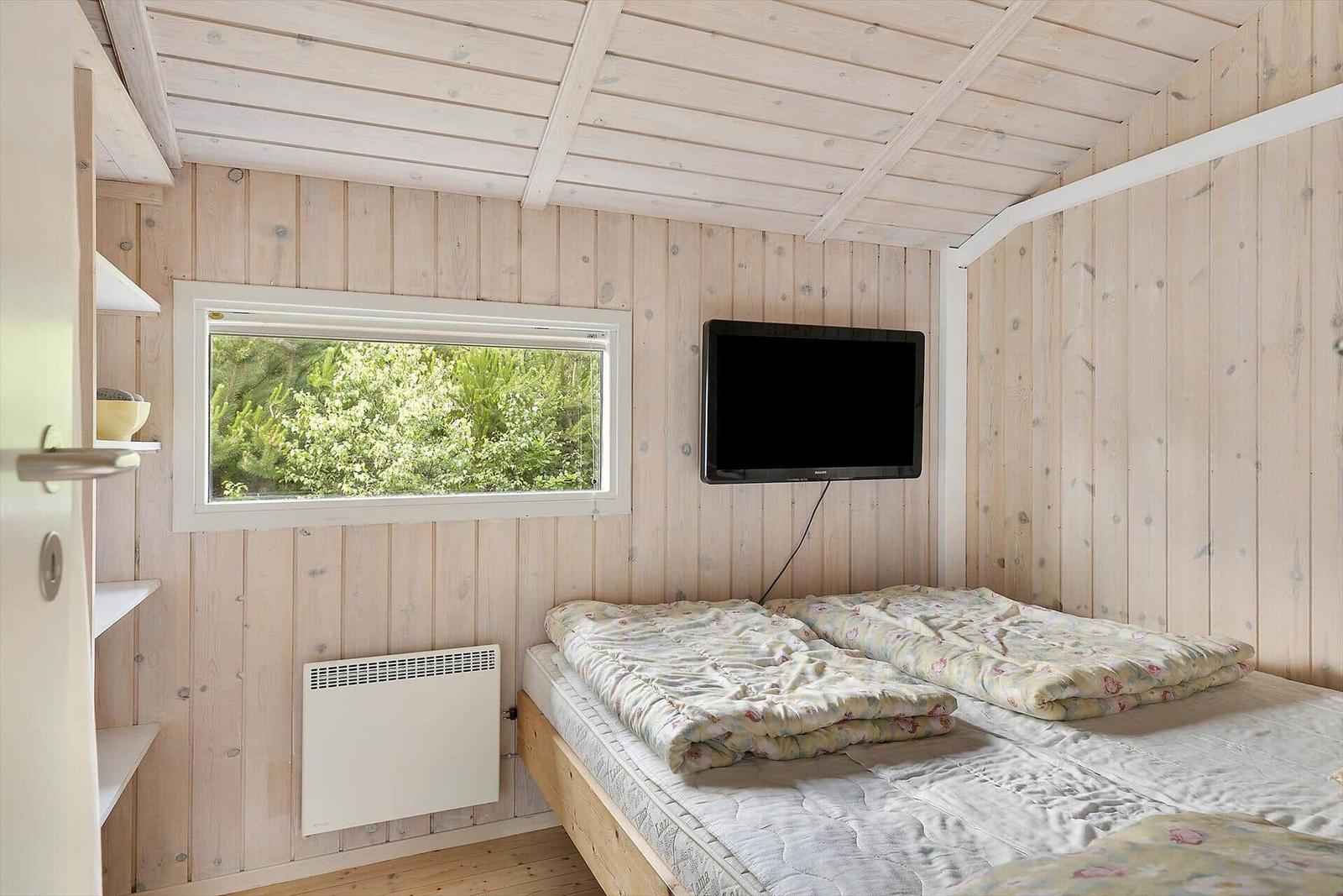 Schlafzimmer mit Bett, Fernseher und Fenster mit Blick auf Grün.