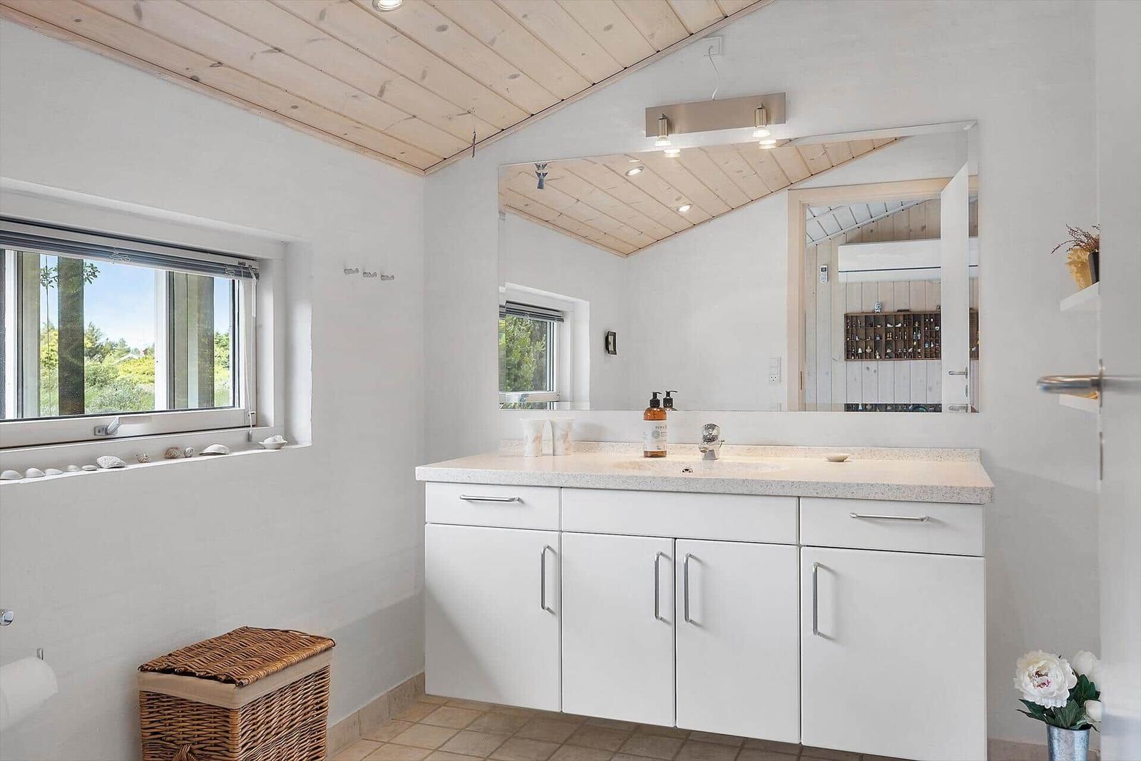 Badezimmer mit Waschbecken, Spiegel und Fenster mit Blick auf Grün.