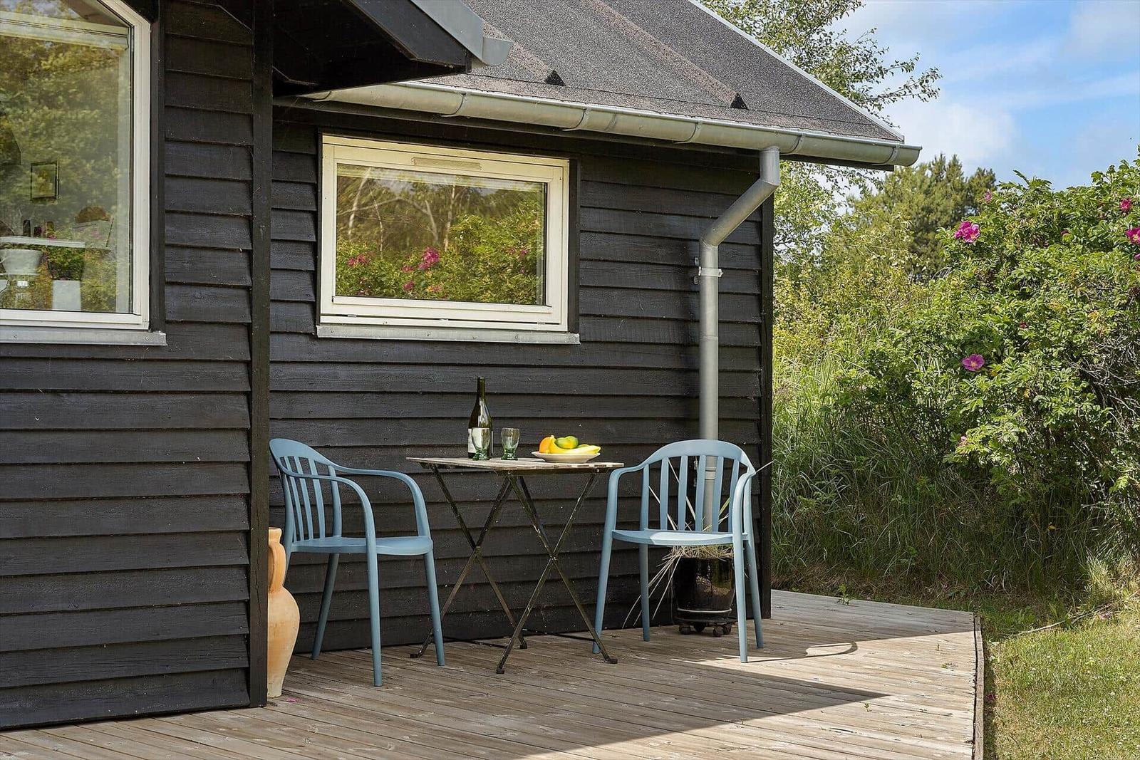 Holzterrasse mit Tisch, zwei Stühlen und Obst vor einem dunklen Holzhaus.