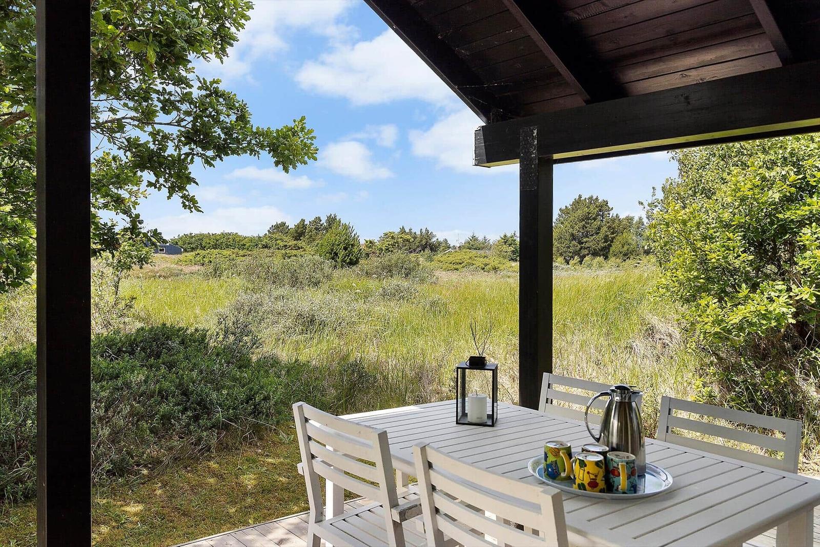 Terrasse mit Tisch und Stühlen, Blick auf grüne Wiese und Bäume.