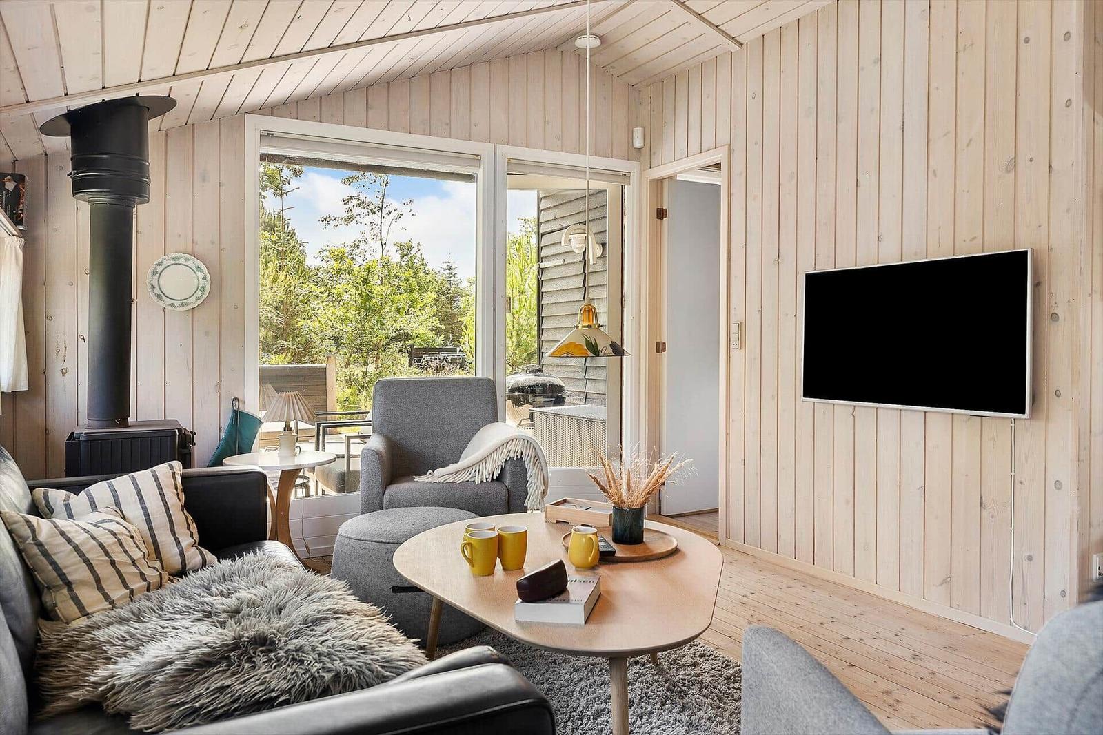 Wohnzimmer mit Holzwand, Sofa, Sessel und Fernseher an der Wand.