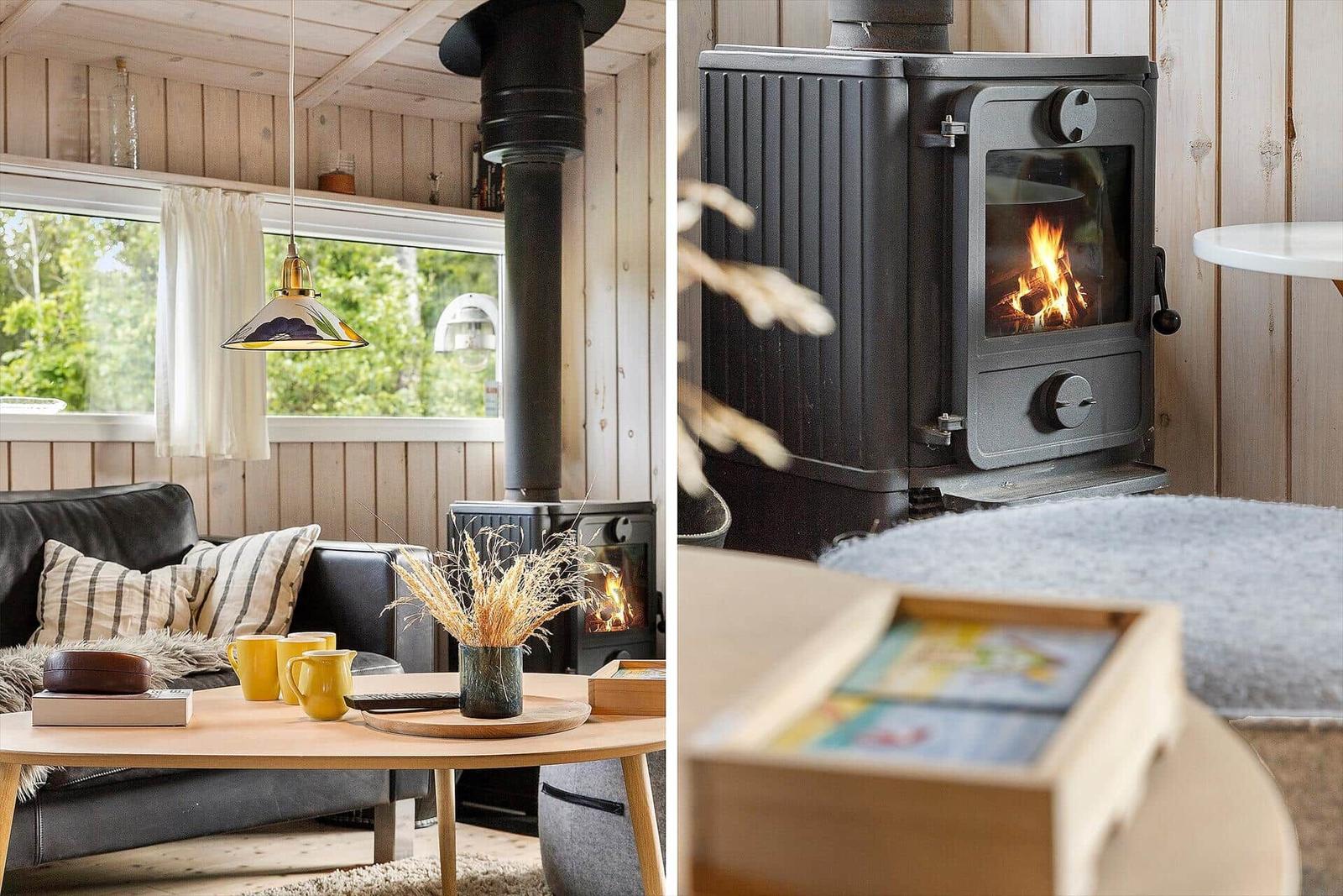 Wohnraum mit Kaminofen, Sofa und Tisch. Holzwände und Fenster mit Blick auf Grün.