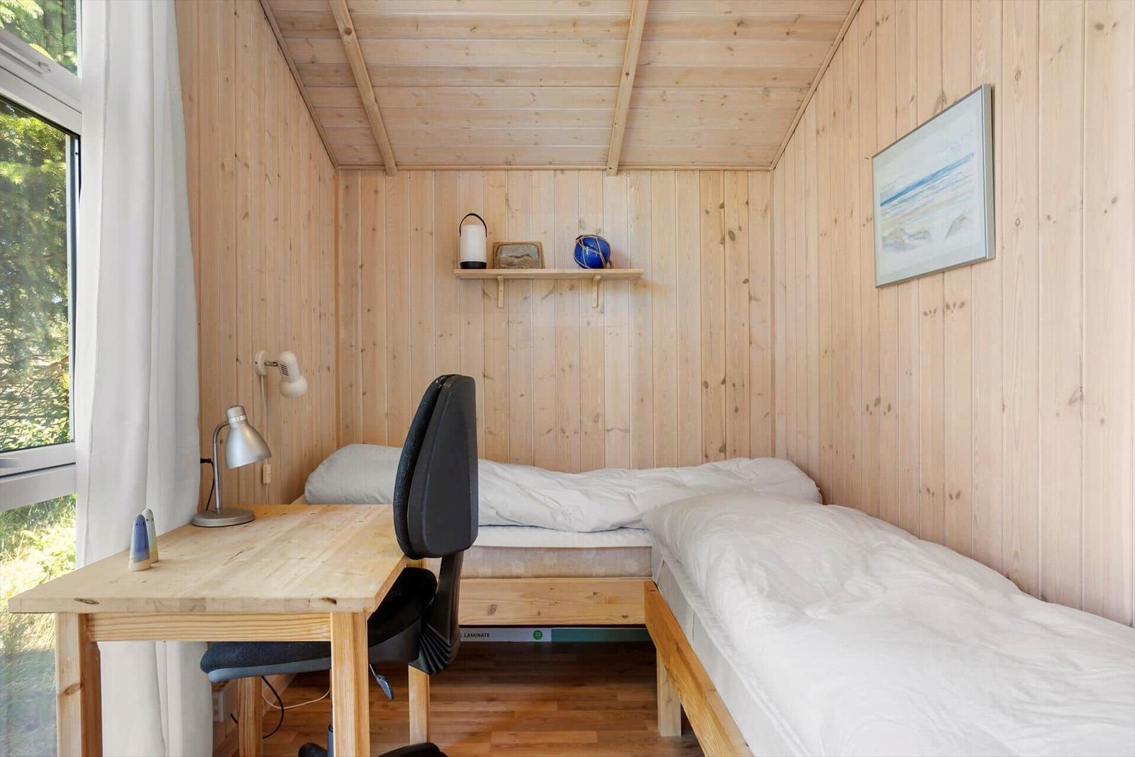 Bedroom with wooden walls, bed, desk, and window.