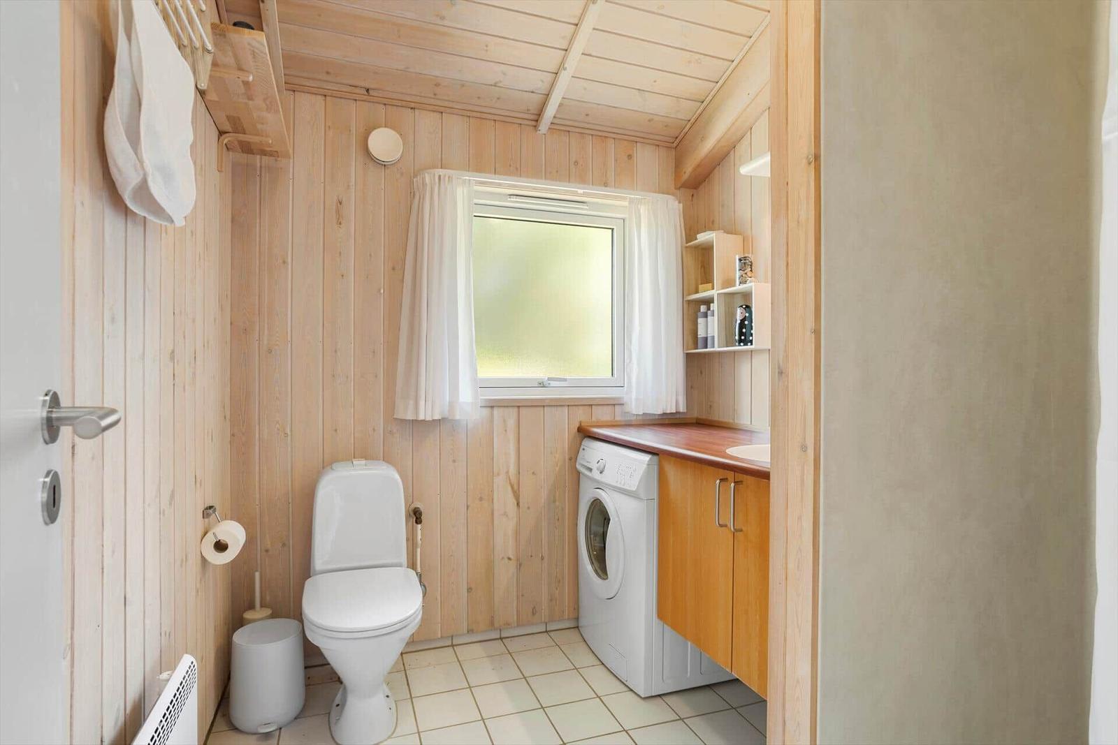 Bathroom with toilet, washing machine, and window with curtains.