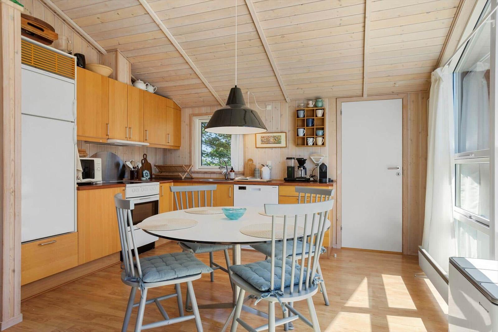 Kitchen with dining area, wooden walls and ceiling, white table and chairs with cushions.