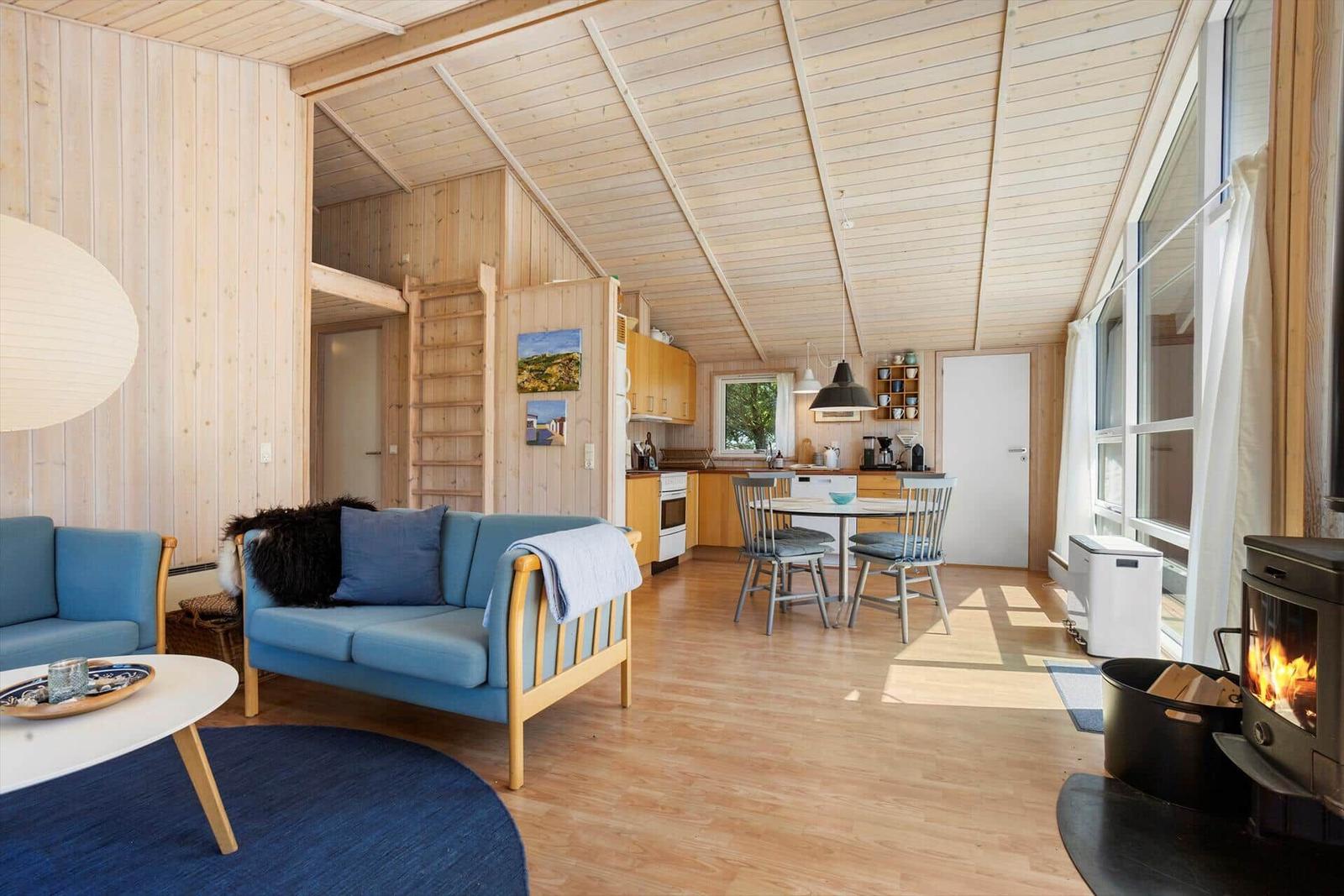 Apartment with wooden ceiling, sofa, dining table, and fireplace.