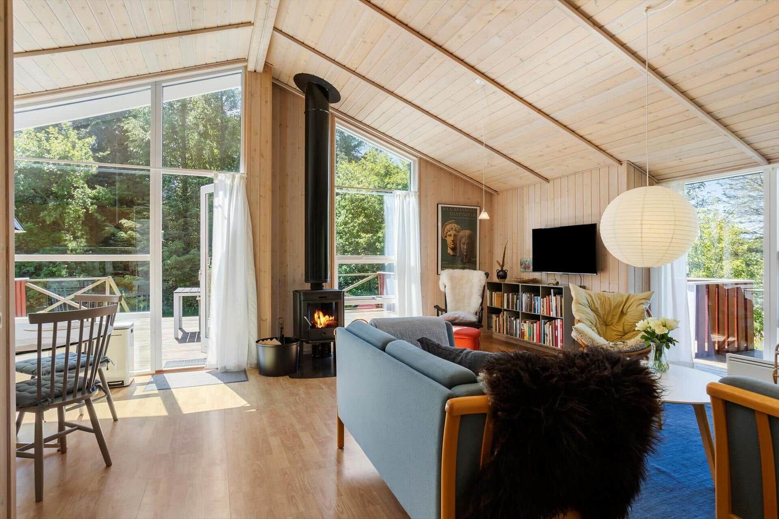 Living room with wooden ceiling, fireplace, and large windows. Furniture and decor are visible.