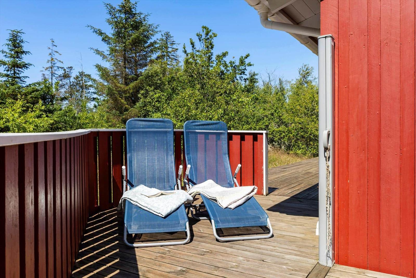 Deck with two blue lounge chairs and view of green trees.