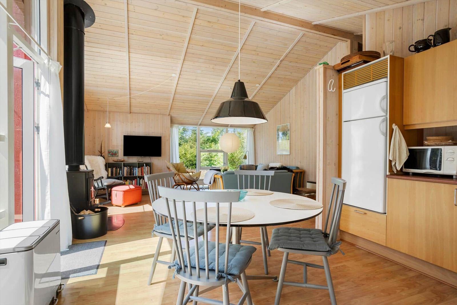 Dining area with table and chairs, kitchen with refrigerator and microwave, wooden ceiling and walls.