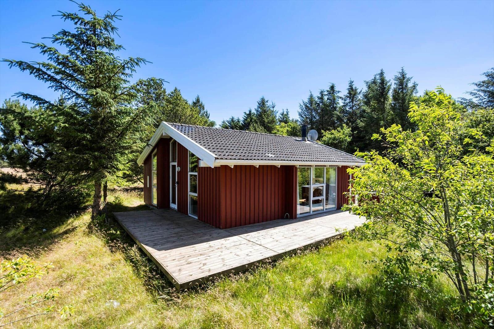 Red wooden house with a deck, surrounded by trees and grass.