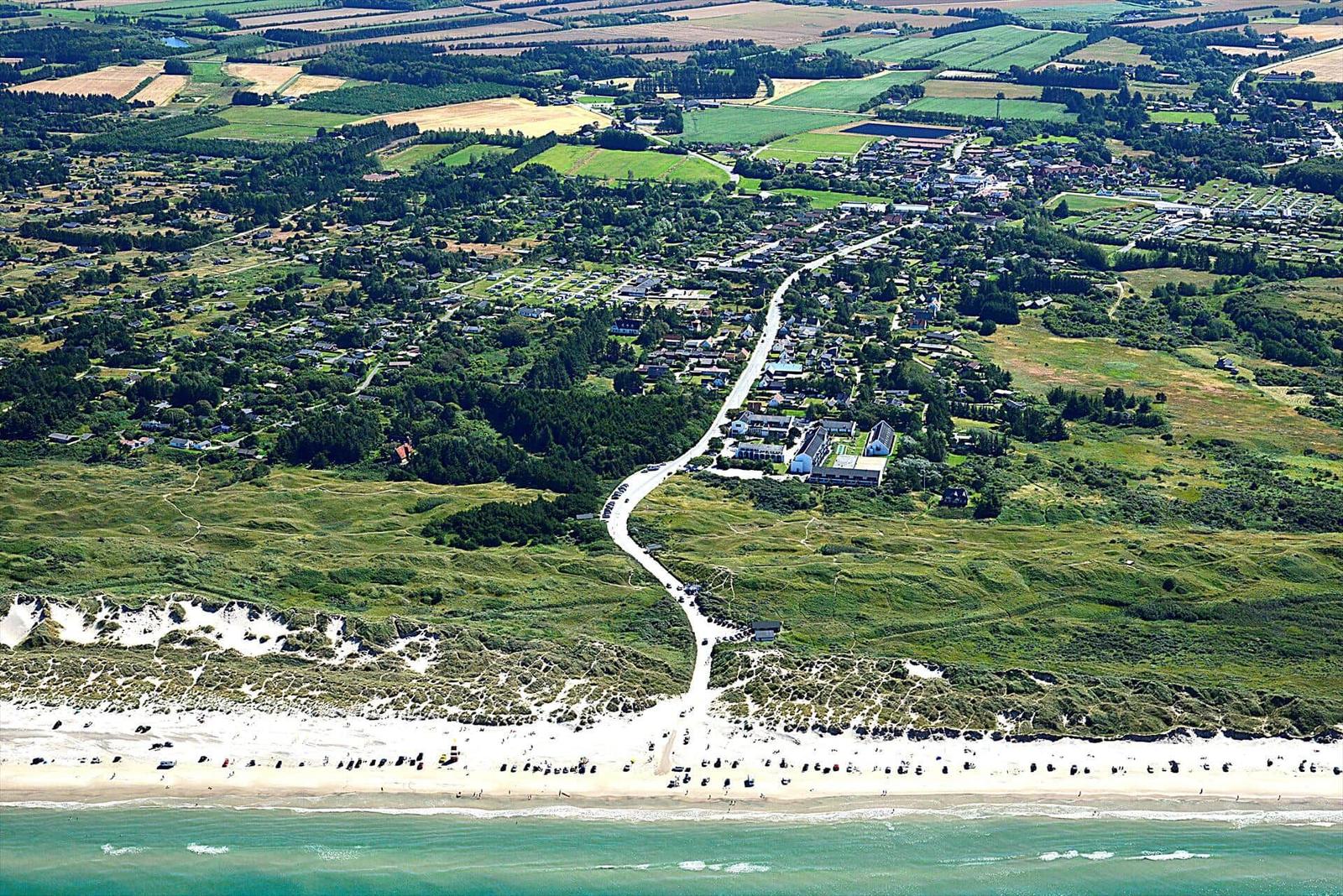 Aerial view of coastal village with beach, dunes, and surrounding green fields.